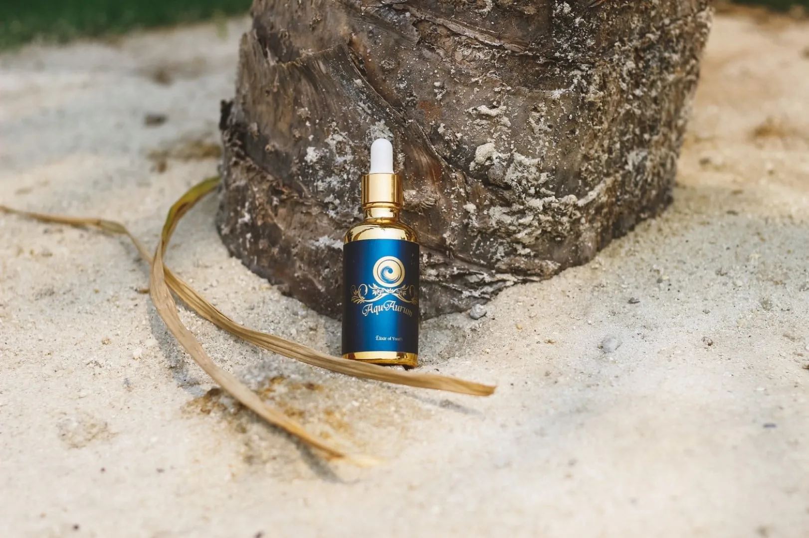 AquAurum bottle arranged on pale sand beside a natural mineral form