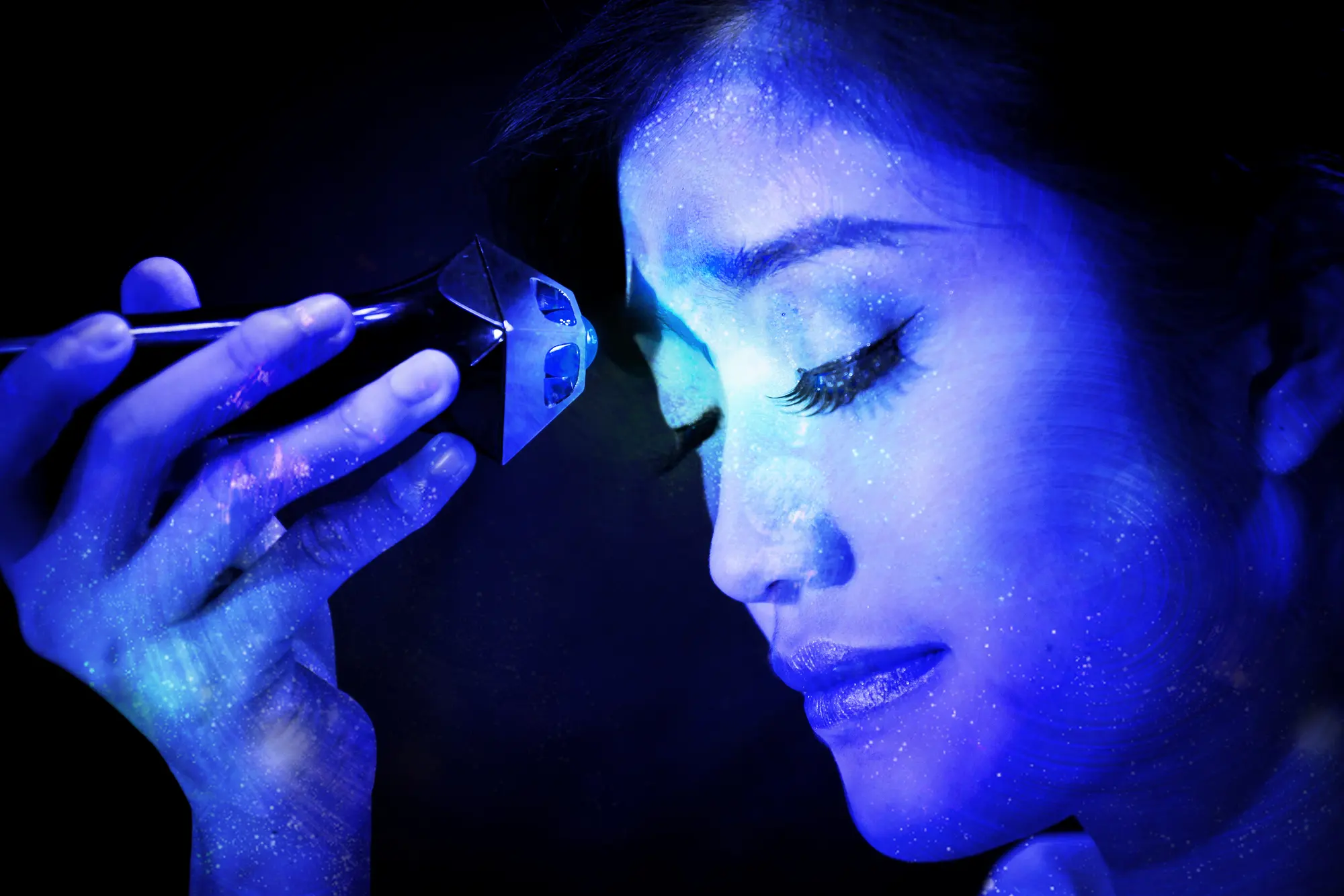 Woman with closed eyes as soft blue light touches her forehead