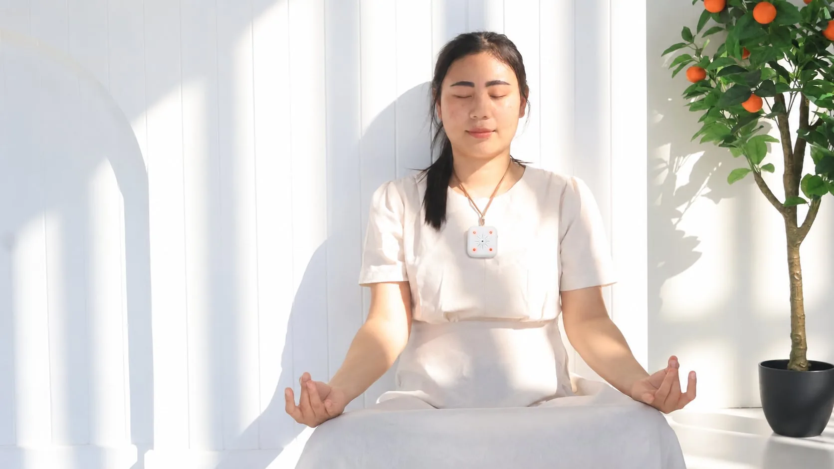 Woman meditating in a sunlit room while wearing Mandala Breeze near her chest