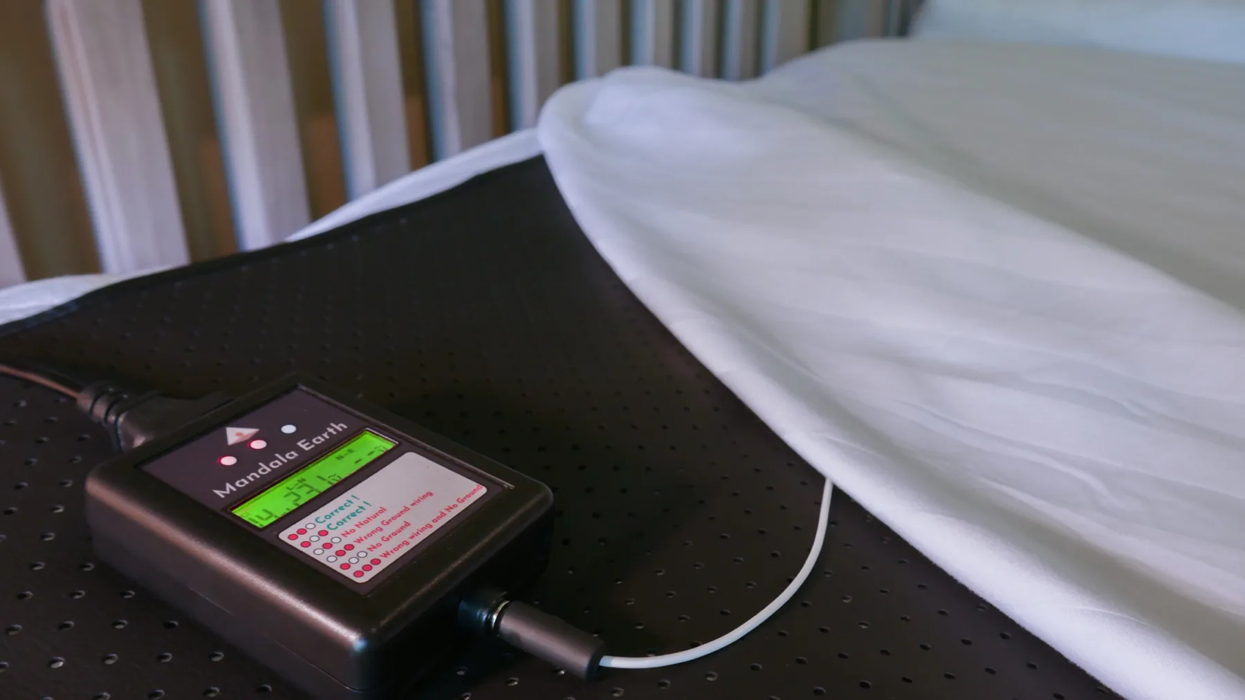 Mandala Earth connection module resting on the conductive mat beneath a folded white bed sheet