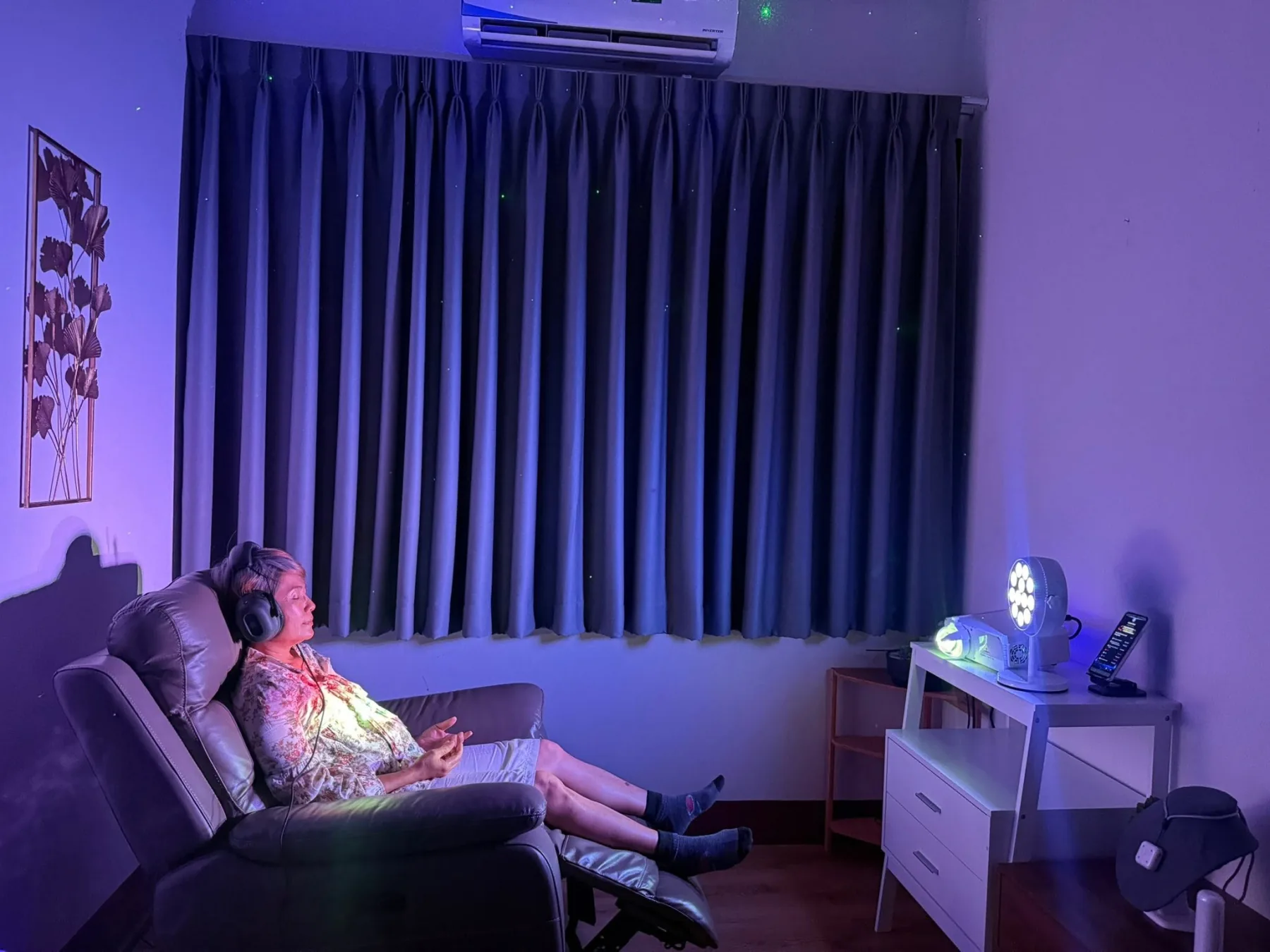 Guest reclining with headphones beside Light Mandalas systems in a blue-lit Wellness Room
